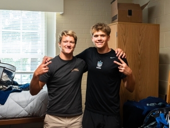 two young men smile together in their dorm room