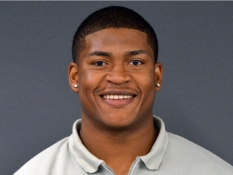Young black man with short hair smiles wearing a grey quarter-zip