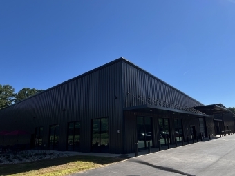 A warehouse-shaped metal building with rows of vertical windows and concrete around the perimeter