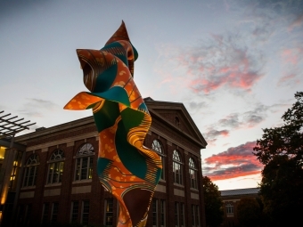 a colorful sculpture in front of an academic building at sunset