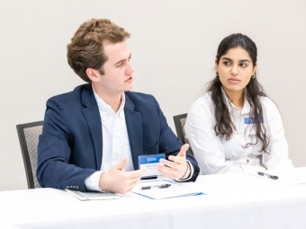 two students discuss at a roundtable while wearing business attire