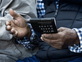 Close up of man's hands holding a program for the With These Hands dedication