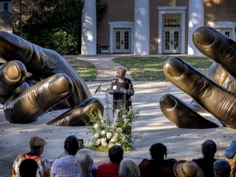 Hilary Green makes remarks at a podium between of the sculpture of the Hands
