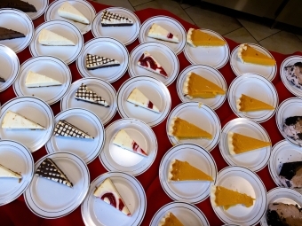 Roughly 30 plates of pie slices on a red tablecloth
