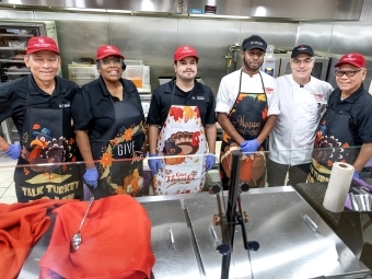 Six employees of Dining Services wear branded Davidson College hats and festive thanksgiving aprons, standing behind the serving counter