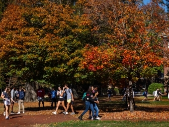 Students wearing backpacks walk past bright autumn foliage on the chambers lawn
