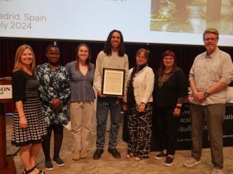students and adults gather around a photo screen and a student holds an award in a frame
