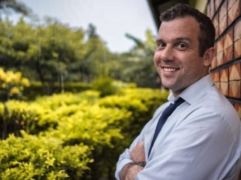 a man in a doctor's jacket smiles leaning against a brick wall