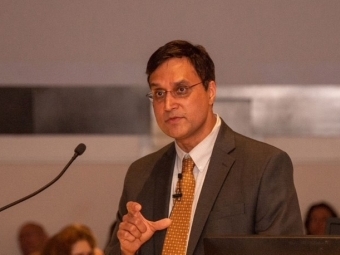 a man wearing a suit and tie speaks into a microphone on stage