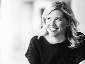 Greyscale image of a smiling white woman, looking to her right, with shoulder length blonde hair