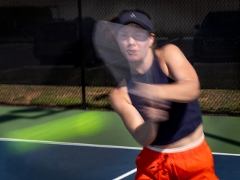 a young woman swings at a pickleball on a court