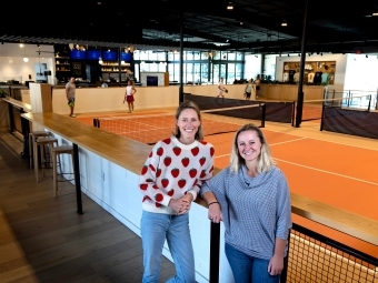 two women stand in front of an indoor pickleball space