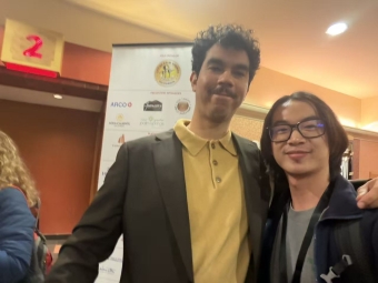 Two men smile for a photo in front of a white banner displaying several event sponsor logos, including the City of Palm Springs.