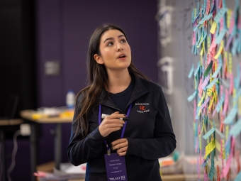 Female student speaks in front of a wall of sticky notes