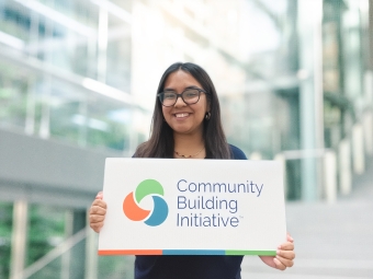 a young woman holds a sign that says "community building initiative"