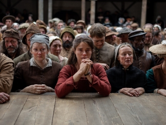 Hamnet movie still of woman with elbows on platform in hopeful gesture