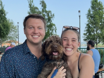 A smiling young couple holding a brown doodle puppy