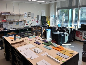 A sunlit printmaking studio filled with papers, presses, and storage for materials