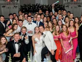 A group of formally dressed people at a wedding, with the bride and groom front and center
