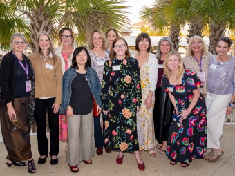 A group of women stand outdoors in front of palm fronts