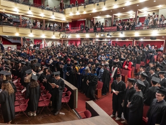 A high-angle view of a large auditorium filled with students and faculty in academic regalia during a convocation ceremony.