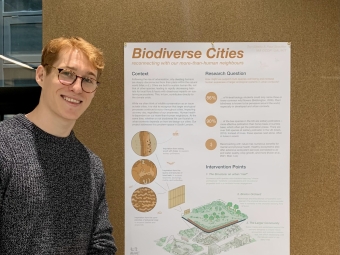 A young man with glasses stands next to a white scientific poster: "Biodiverse Cities"