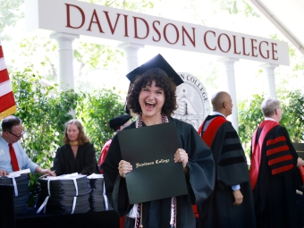 Student beams holding her diploma onstage