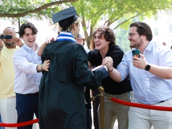 A male student receives a pat on the back from three friends at commencement