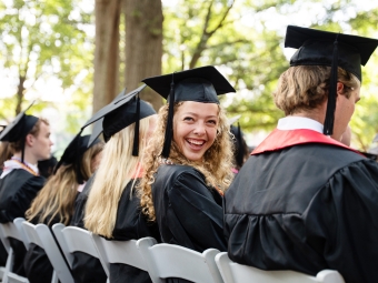 A blonde, curly-haired student turns around in her seat and smiles during commencement