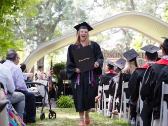 A female student in a graduation robe walks back to her seat after receiving her diploma