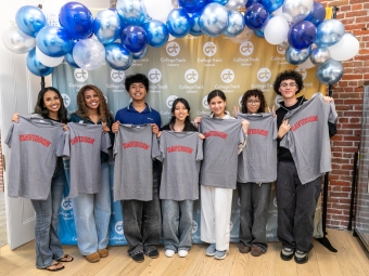 Seven smiling students stand in a row in front of a College Track Oakland backdrop and a blue and white balloon arch, each holding up a grey T-shirt with the word "DAVIDSON" printed in red arched lettering.