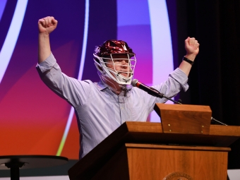 Doug Hicks speaking at the 2026 Employee Appreciation event wearing a lacrosse helmet