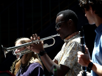 A close-up shot of a student playing a silver trumpet alongside other musicians in a dimly lit performance space.