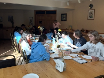 A table of students in blue sweatshirts and casual clothing enjoying dinner