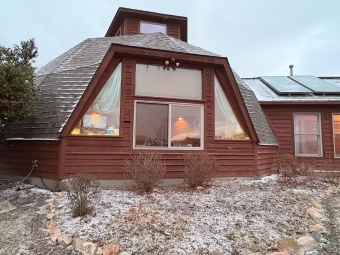 A hexagonal wooden cabin with large windows and a snowy front bed