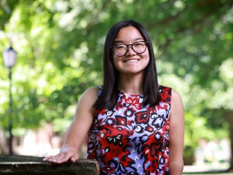 A smiling student with glasses and straight, dark hair poses outside wearing a sleeveless floral patterned blouse.