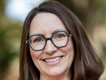 A woman with shoulder-length brown hair and glasses and a bright purple shirt