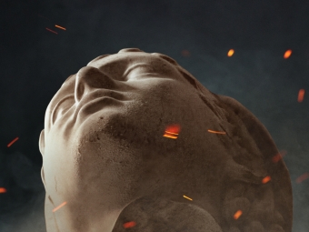 Close-up, low-angle view of a stone classical bust tilted backward against a dark, smoky background with floating orange embers
