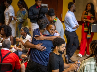 Two men embrace warmly in a hug amidst a crowded indoor reception room.