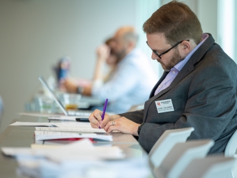 A man with glasses at a table at an event writes notes