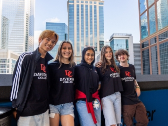 Five students in black and red Davidosn College shirts, with skyscrapers in the background