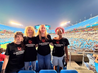 Four students stand in the stands, in front of the field at Charlotte FC