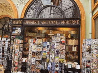 The front display of an antique bookstore named "Reliure Librairie Ancienne & Moderne" filled with revolving racks of postcards and rows of old books.