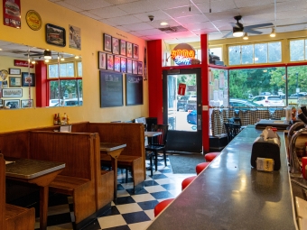The interior of an old fashioned soda shop, with red bar stools, black and white checkerboard tiled floor, and wooden booths lining the wall