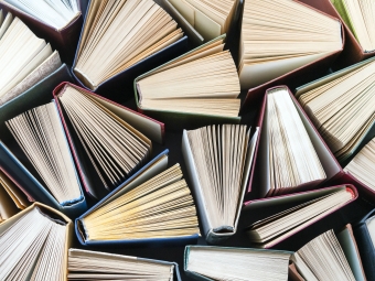 An overhead, top-down view of dozens of hardcover books arranged tightly together, each standing partially open with their paper pages fanning outward to form a geometric pattern.
