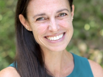 A smiling woman with brown shoulder length hair and a teal sleeveless blouse