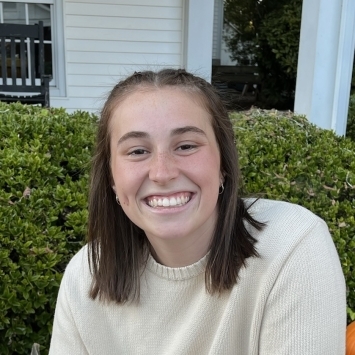a young white woman with brown hair wearing a white sweater