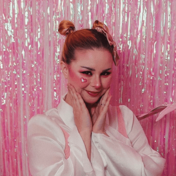 a young white woman smiling in front of a pink wall