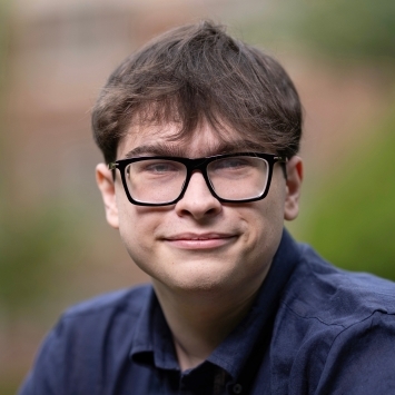 a young white man with brown hair wearing black glasses and a blue collared shirt