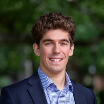 a young white man with curly brown hair wearing a collared shirt and jacket